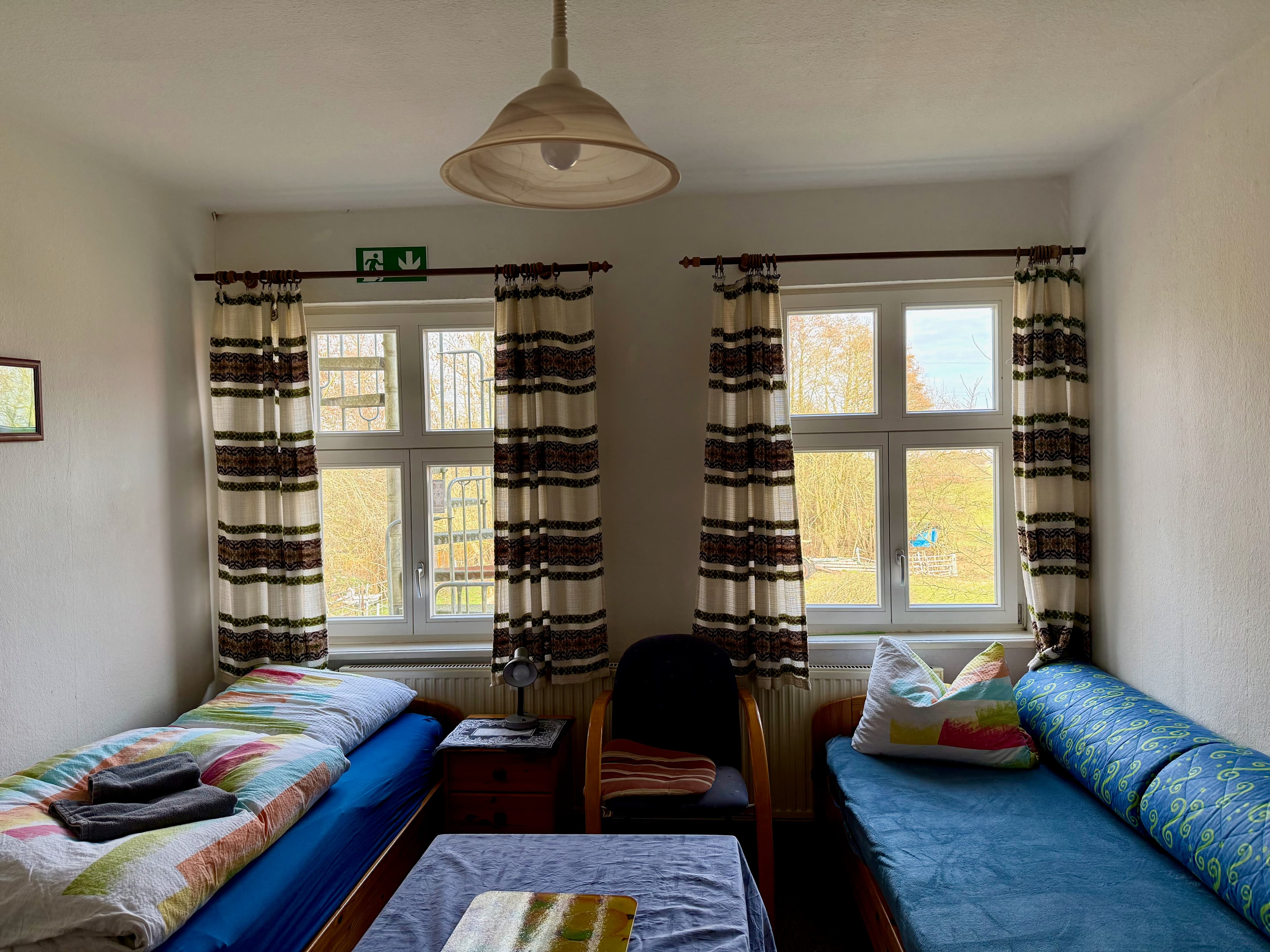 Zimmer mit zwei getrennten Betten, Tisch und großen Fenstern