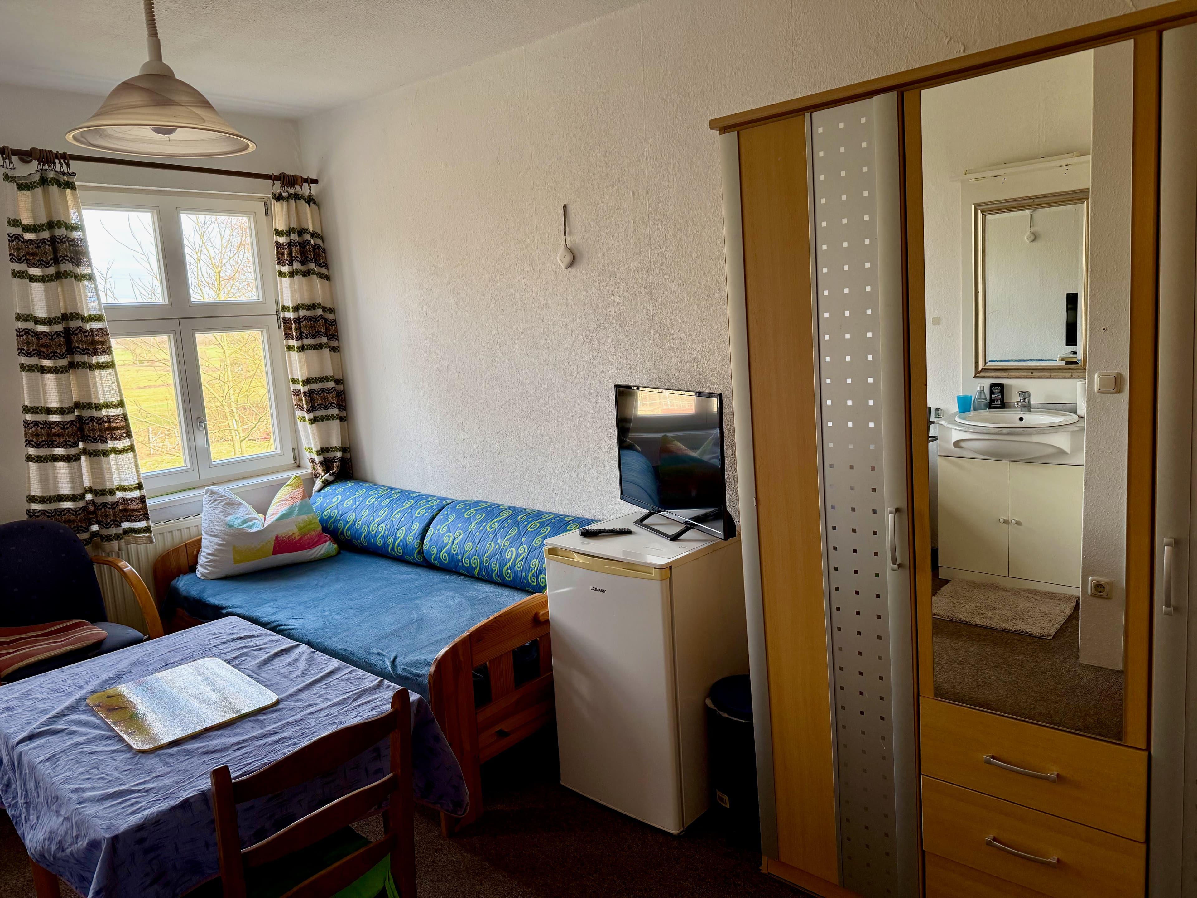 Einfaches Gästezimmer mit Bett, Kühlschrank, Schrank und Waschbecken