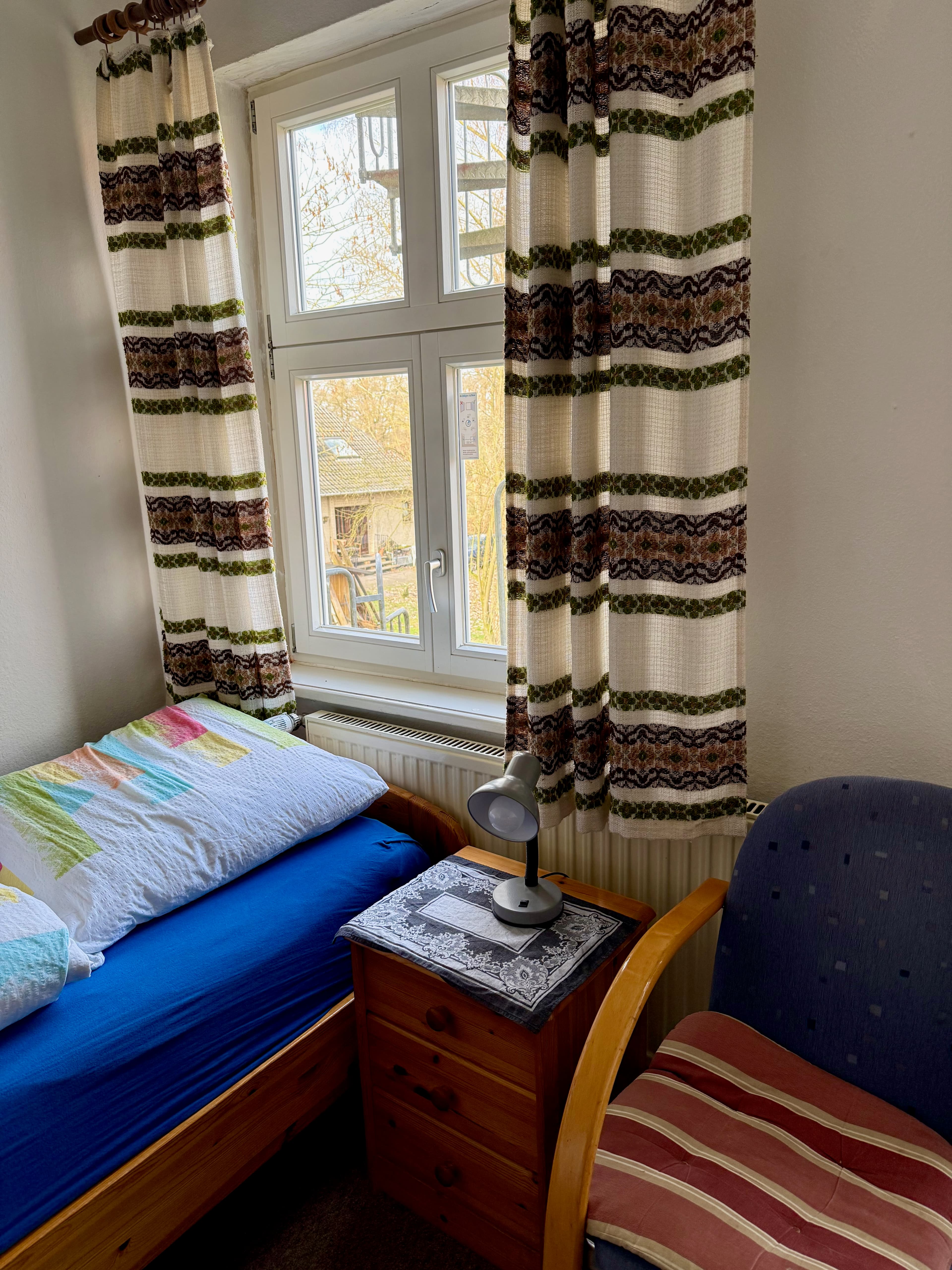 Einzelbett mit Nachttisch und Sitzplatz am Fenster