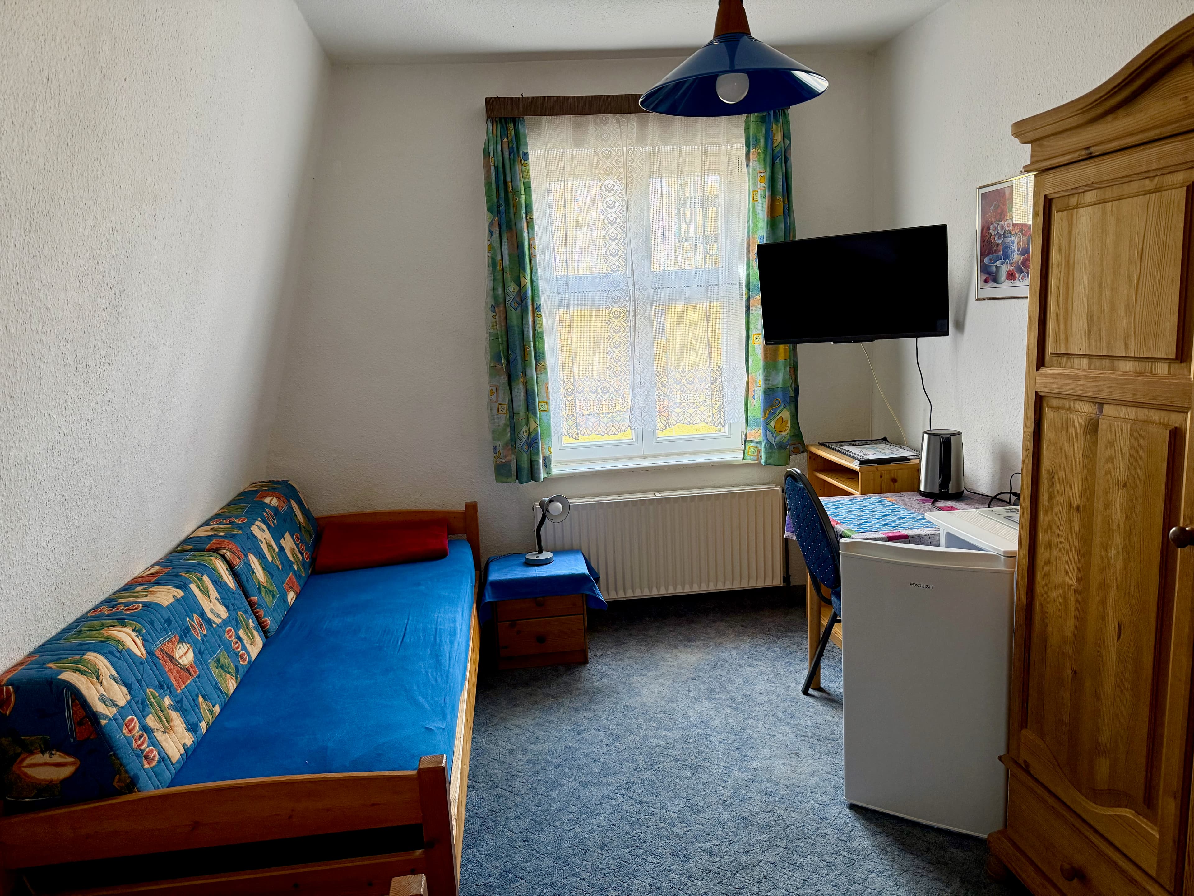 Einzelzimmer mit Bett, Kühlschrank und kleinem Arbeitsplatz