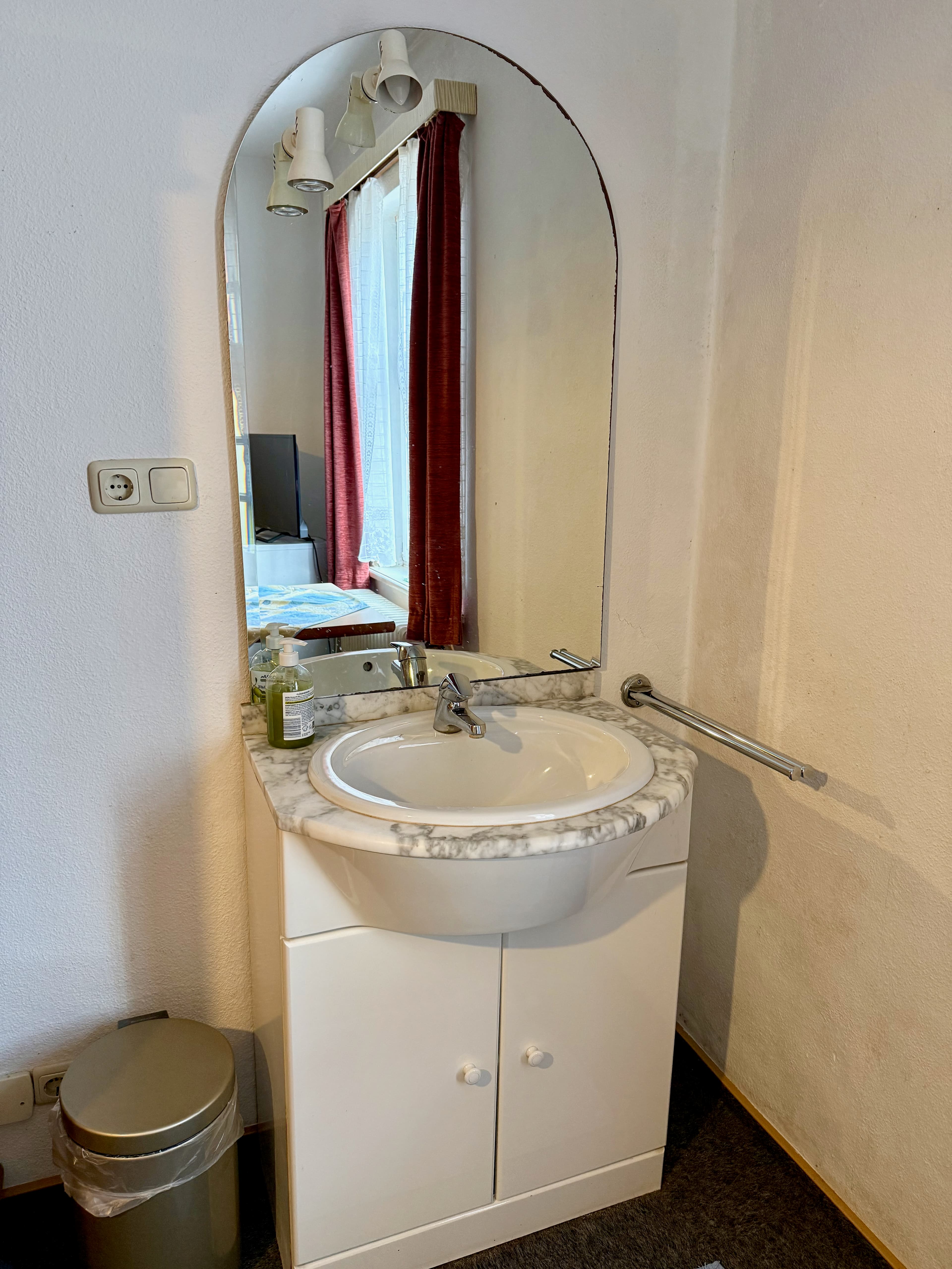 Einzelzimmer mit Bett, Kühlschrank und kleinem Arbeitsplatz