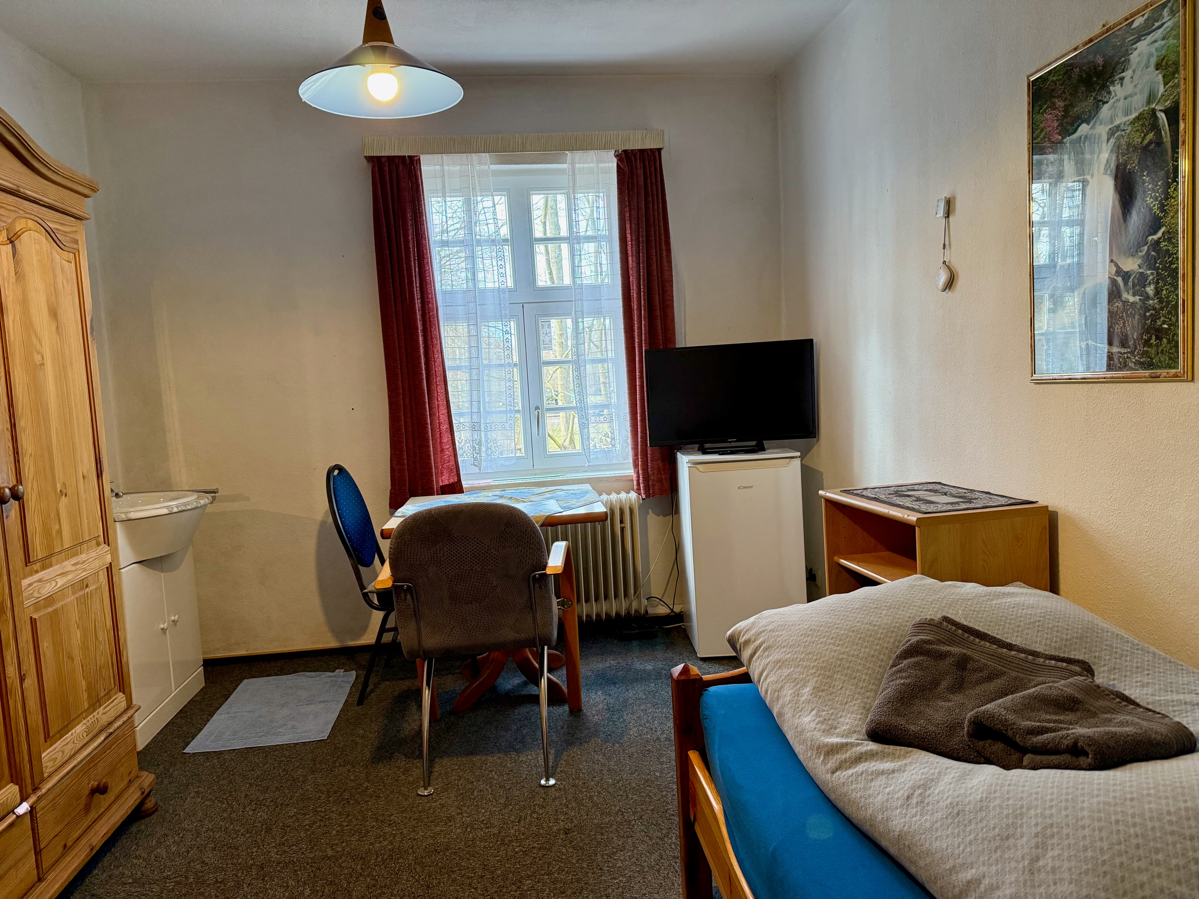 Einzelzimmer mit Bett, Tisch, Fernseher und Kühlschrank
