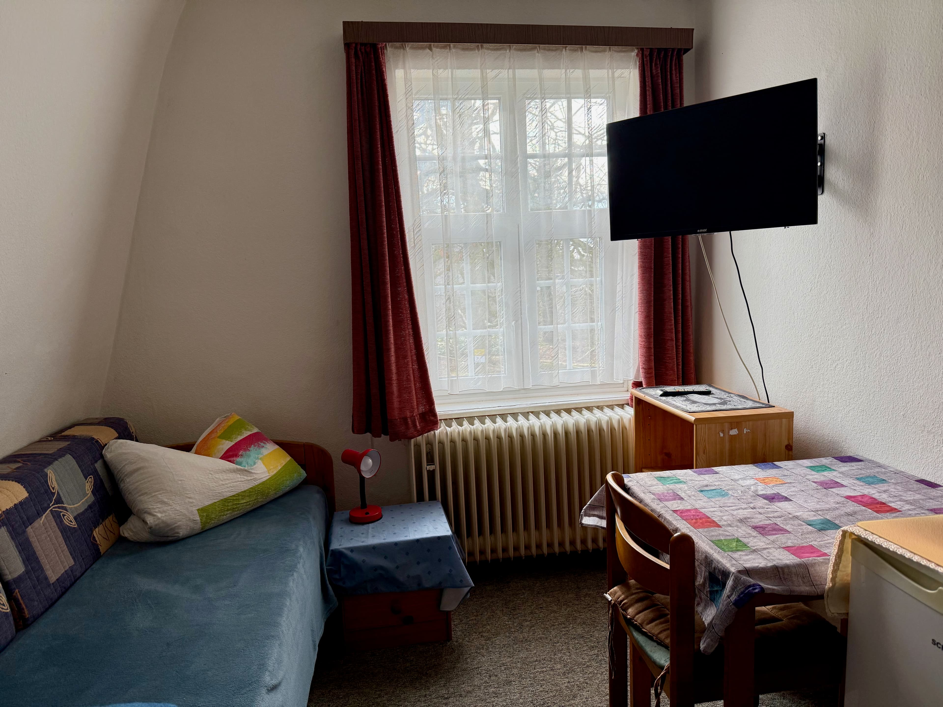 Einzelzimmer mit Bett, Tisch, Fernseher und Kühlschrank